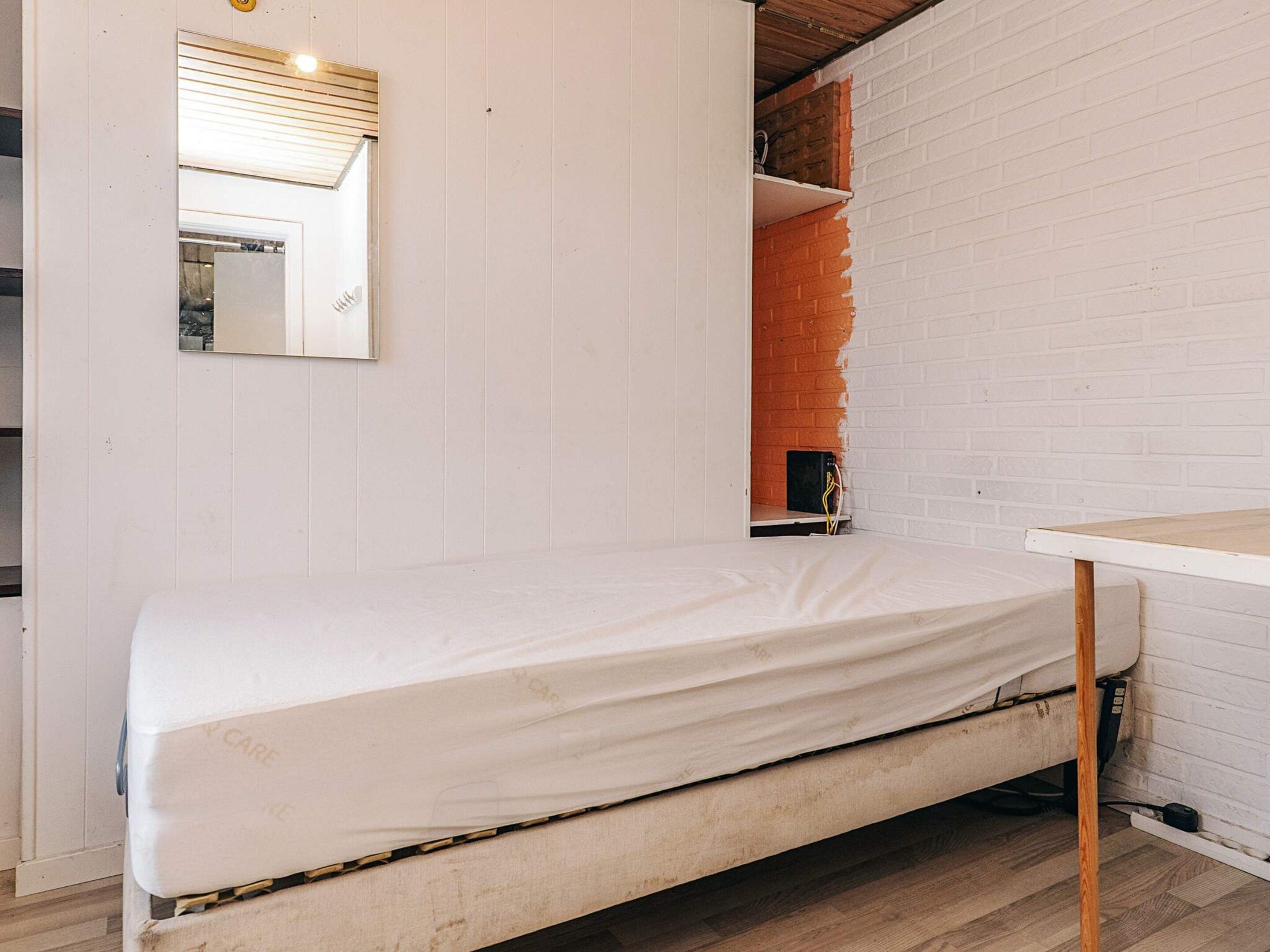 Een eenpersoonsbed met een witte matras in een kamer met witte wanden en een houten vloer.