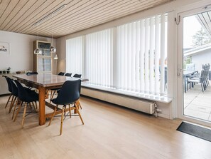 Un'area pranzo moderna con tavolo e sedie in legno, ampie finestre con tende e vista all'esterno.