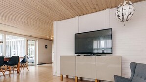 Een moderne woonkamer met een flatscreen televisie, een grijze bank, een houten salontafel en een eethoek met stoelen en een tafel.