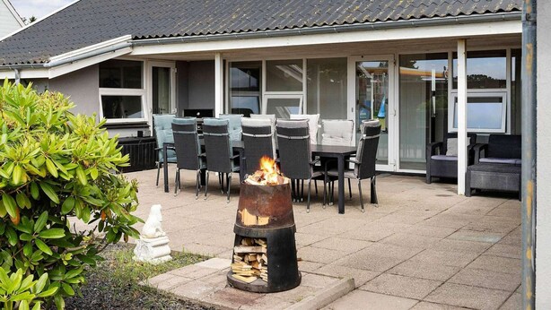 Een overdekt terras met buitenmeubilair, een vuurkorf en uitzicht op het huis.