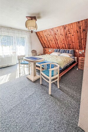 A bedroom with a sloped ceiling, a bed with multiple pillows, a small table with chairs, and a window with curtains. - Wonderful private villa for 7 people with WIFI, TV and pets allowed (Chodov)