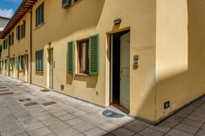 Reihenweise gelbe Häuser mit grünen Fensterläden, einem gefliesten Gehweg und einer Tür mit einer Hausnummer.