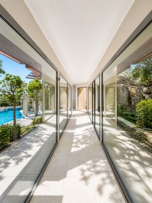 Un pasillo moderno con paredes de cristal que conduce a una zona de piscina con vista a un paisaje rocoso.