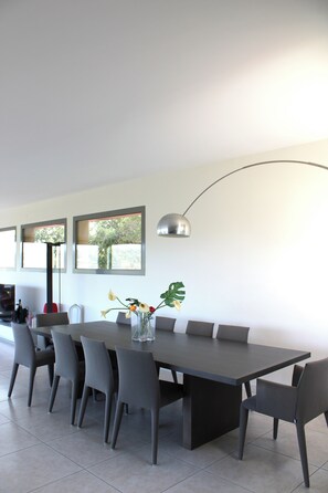 Un comedor moderno con una mesa larga, seis sillas, un jarrón con flores y una lámpara colgante.