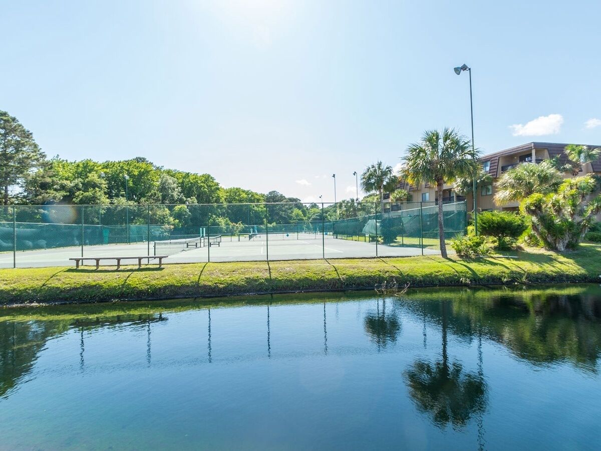 En fredfyldt park med tennisbane, bænke og et roligt vandareal.