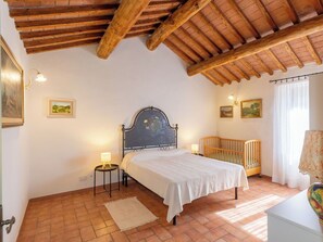 Ein Schlafzimmer mit einem Bett, einem Babybett, einem kleinen Tisch mit Lampe und einem Bild an der Wand.