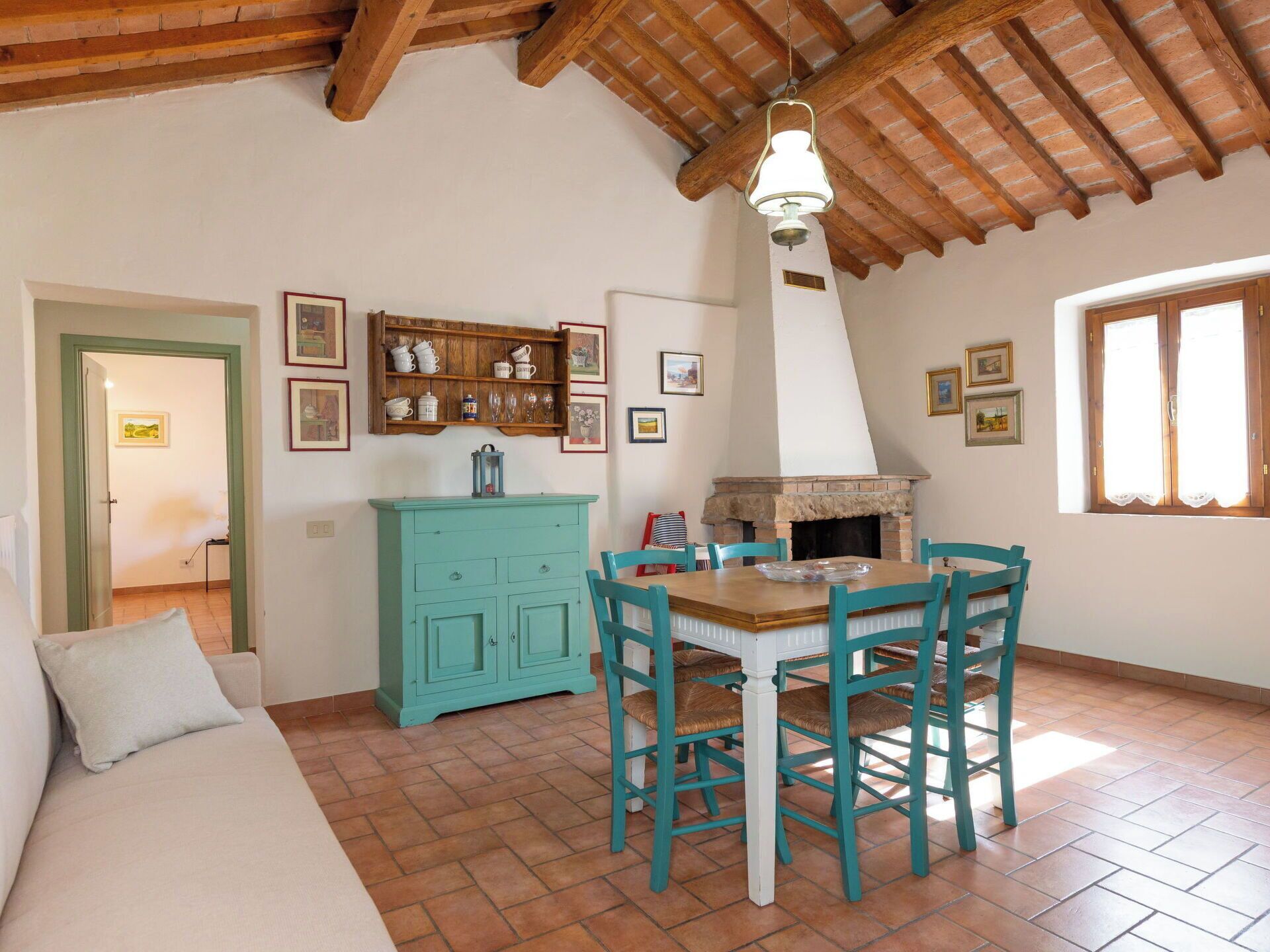 Une cuisine chaleureuse avec un plafond en bois, une table à manger avec des chaises, un meuble de couleur turquoise et une cheminée.