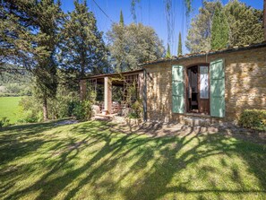 A stone house with a covered patio, a wooden door, and a view of a green field. - Beautiful apartment for 4 people with WIFI, patio and pets allowed (Riparbella)