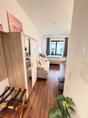 A modern living room with a sofa, a wooden floor, a plant, and a view through a window. - Fewo Mia | cozy city apartment for 4 people - ideal for families (Bamberg)