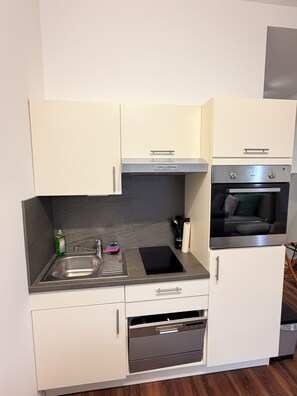 A compact kitchen with a sink, stove, oven, and white cabinets. - Fewo Mia | cozy city apartment for 4 people - ideal for families (Bamberg)