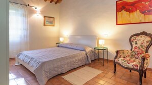 A bedroom with a bed, two bedside tables with lamps, a chair, a painting, and a window with curtains. - Lovely apartment for 5 people with WIFI, patio and pets allowed (Riparbella)