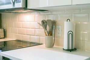 A kitchen counter with a white paper towel holder, a container with kitchen utensils, and a power outlet. - Royal 2BR Sleeps 9, Downtown, Free Valet Parking (Dallas)