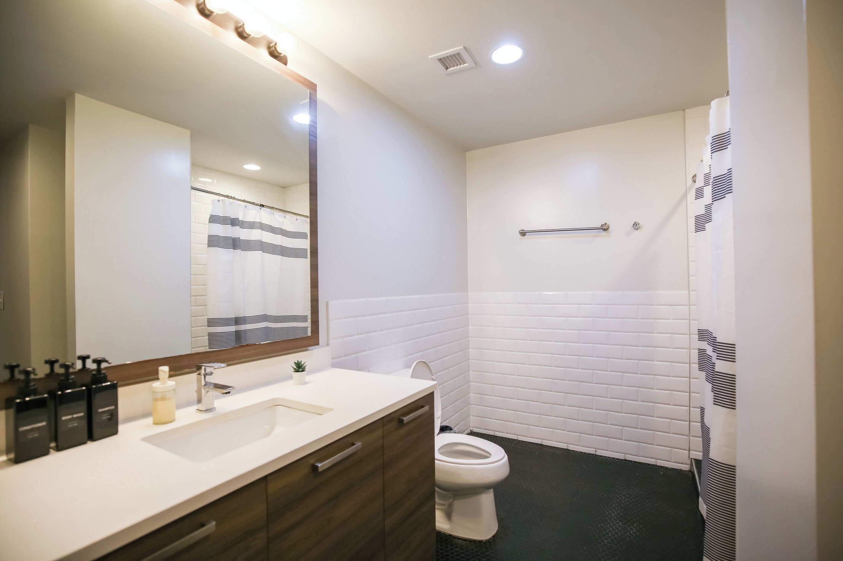 A modern bathroom with a white sink, mirror, and toilet. There are toiletries on the sink, and a shower curtain with a striped pattern.