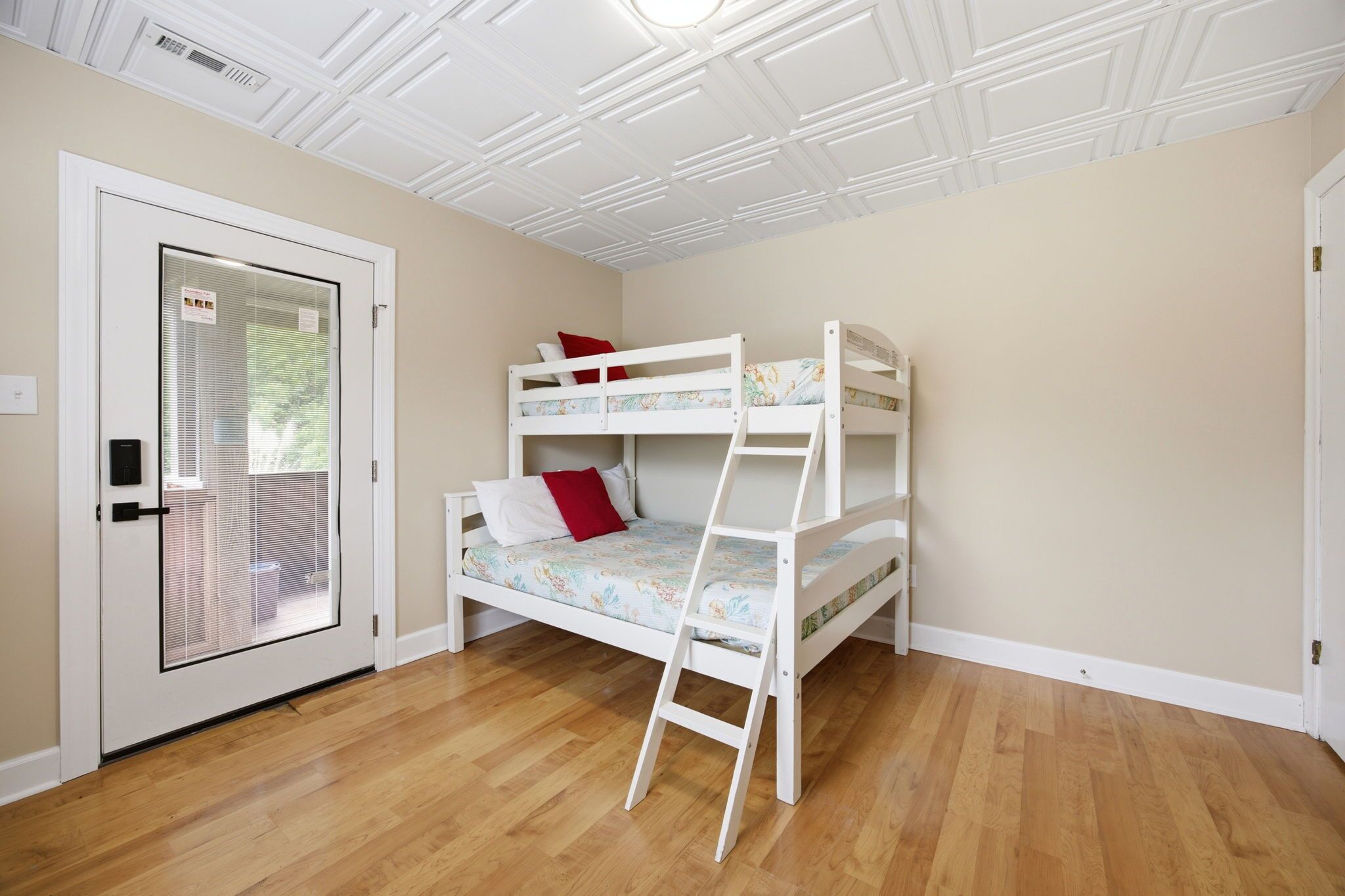 A room with a bunk bed, a door with a window, and a wooden floor.