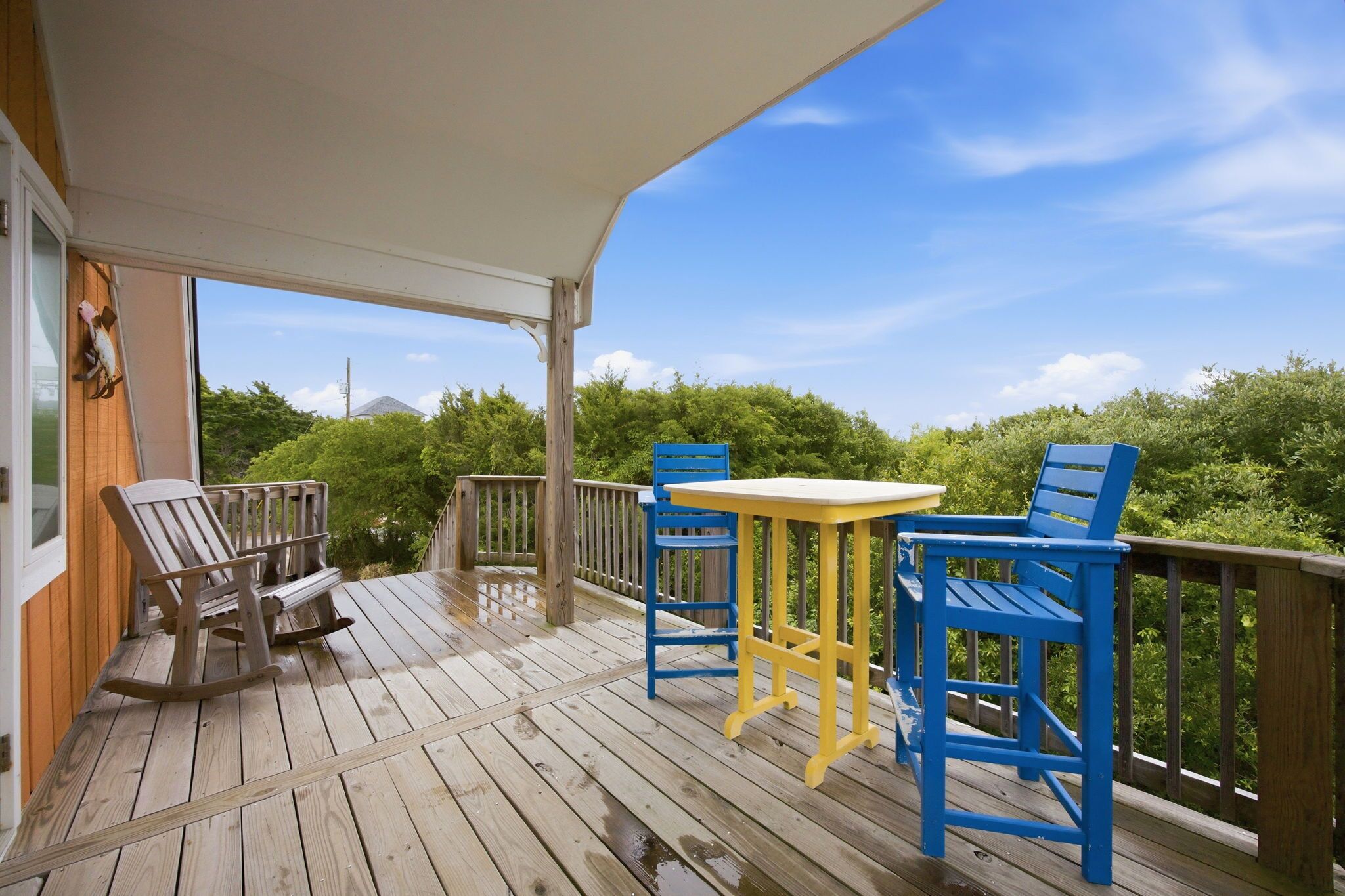 A wooden deck with a covered area, two rocking chairs, and a table with chairs.