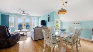 Ein Wohnzimmer mit Glastisch, weißen Stühlen, Deckenventilator und Fernseher.