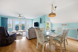 A living room with a glass table, white chairs, a ceiling fan, and a TV. - Dog Friendly, Beach Home, Private Pool- 400ft to beach! (Emerald Isle)