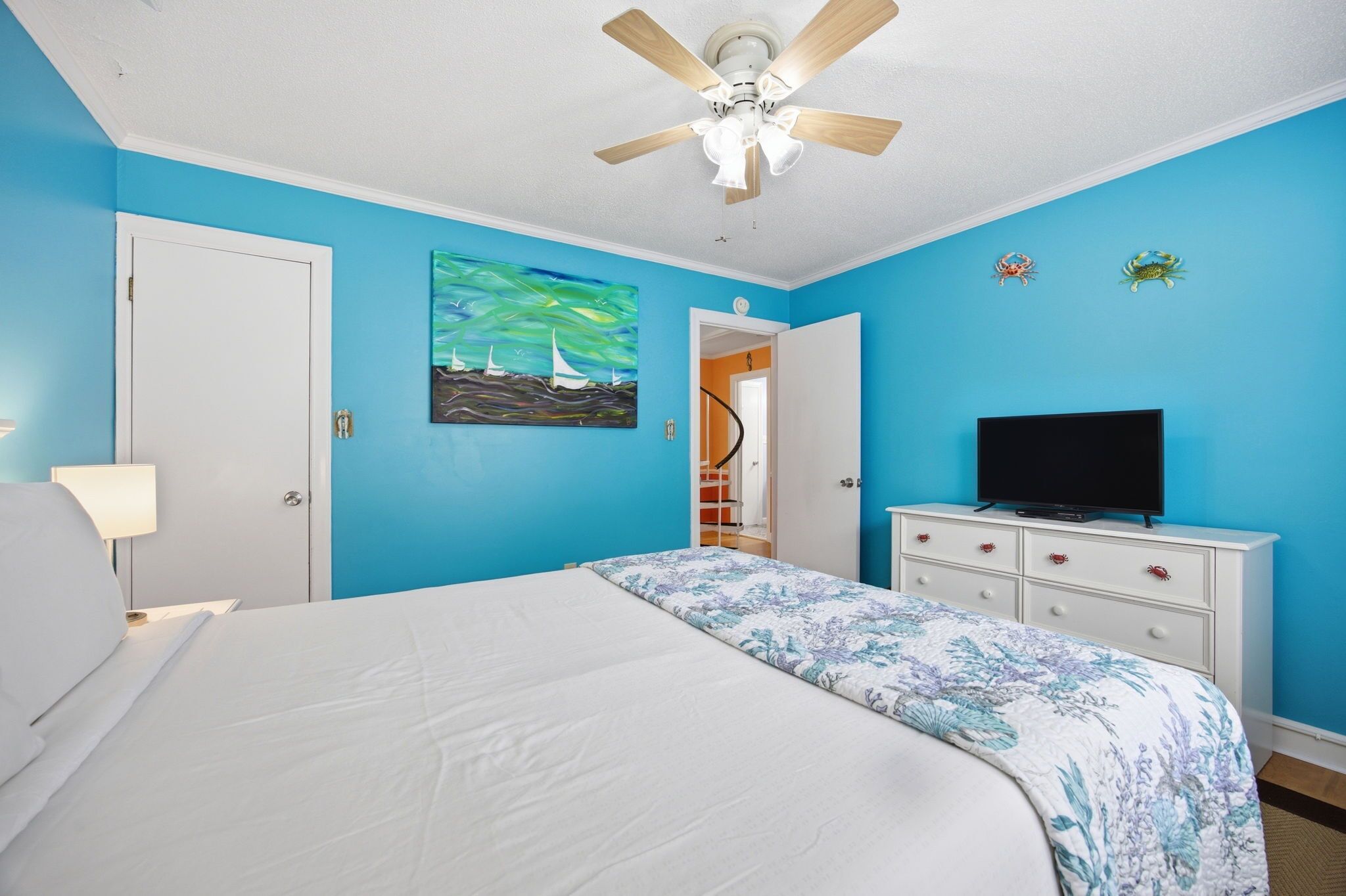 A bedroom with a bed, a ceiling fan, a TV on a dresser, and a painting on the wall.
