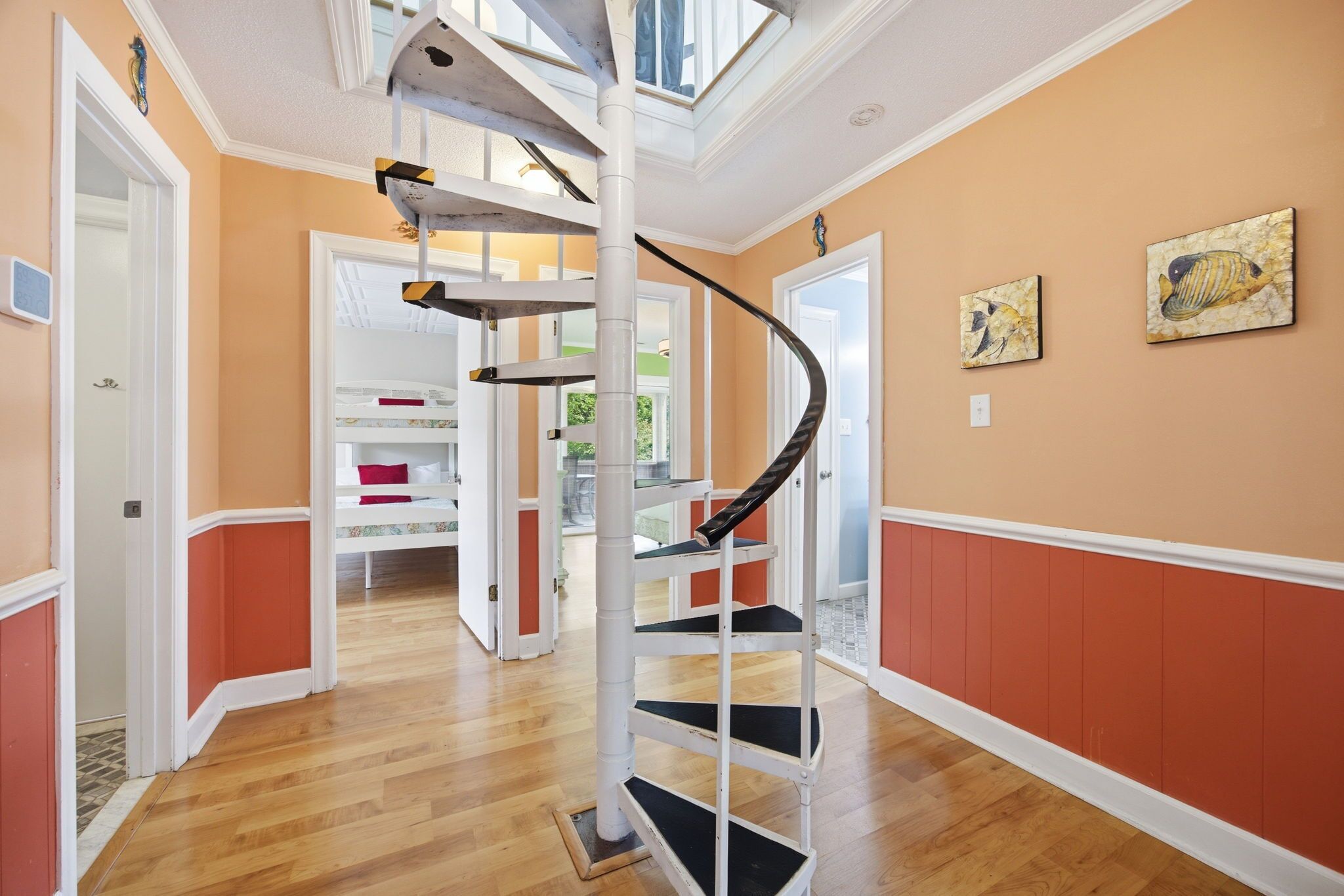 A spiral staircase with a glass enclosure, wooden flooring, and a view of a room with a bed and a red pillow.