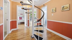 Eine Wendeltreppe mit Glasumrandung, Holzboden und Blick auf einen Raum mit einem Bett und einem roten Kissen.
