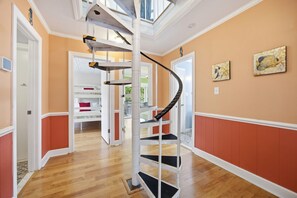A spiral staircase with a glass enclosure, wooden flooring, and a view of a room with a bed and a red pillow. - Dog Friendly, Beach Home, Private Pool- 400ft to beach! (Emerald Isle)