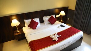 Habitación de hotel con una cama grande, dos lámparas de noche, una colcha roja y blanca y una toalla blanca sobre la cama.
