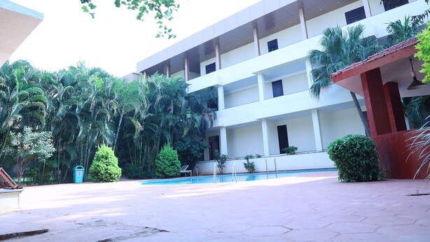 Un edificio de varios pisos con piscina, rodeado de vegetación y palmeras.