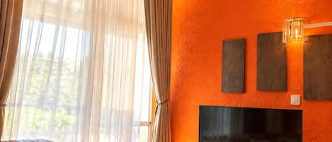 A modern living room with a sofa, a coffee table, and a TV against an orange wall.