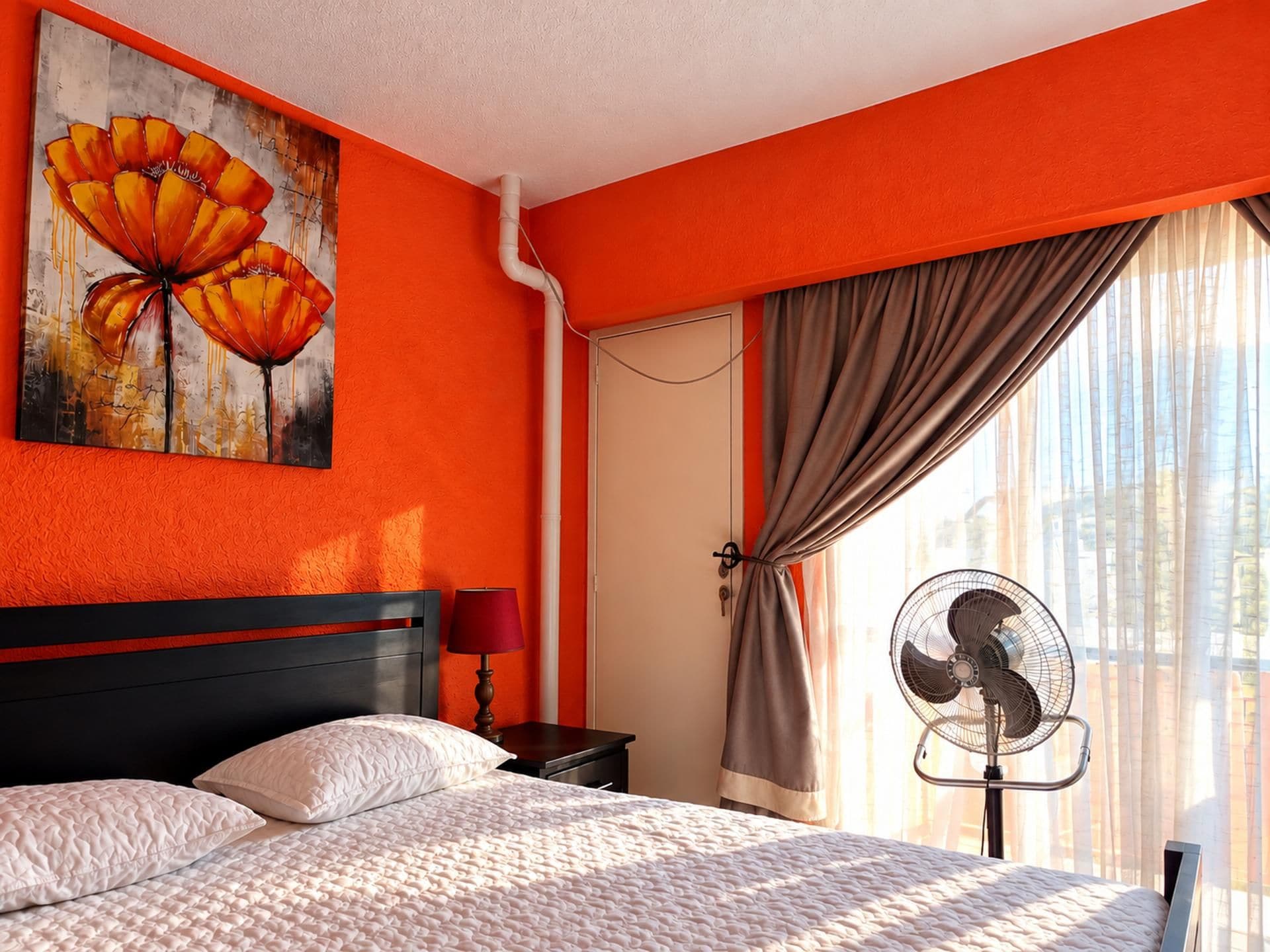 Una habitación de hotel con una cama, un cuadro, un ventilador y una ventana con cortinas.