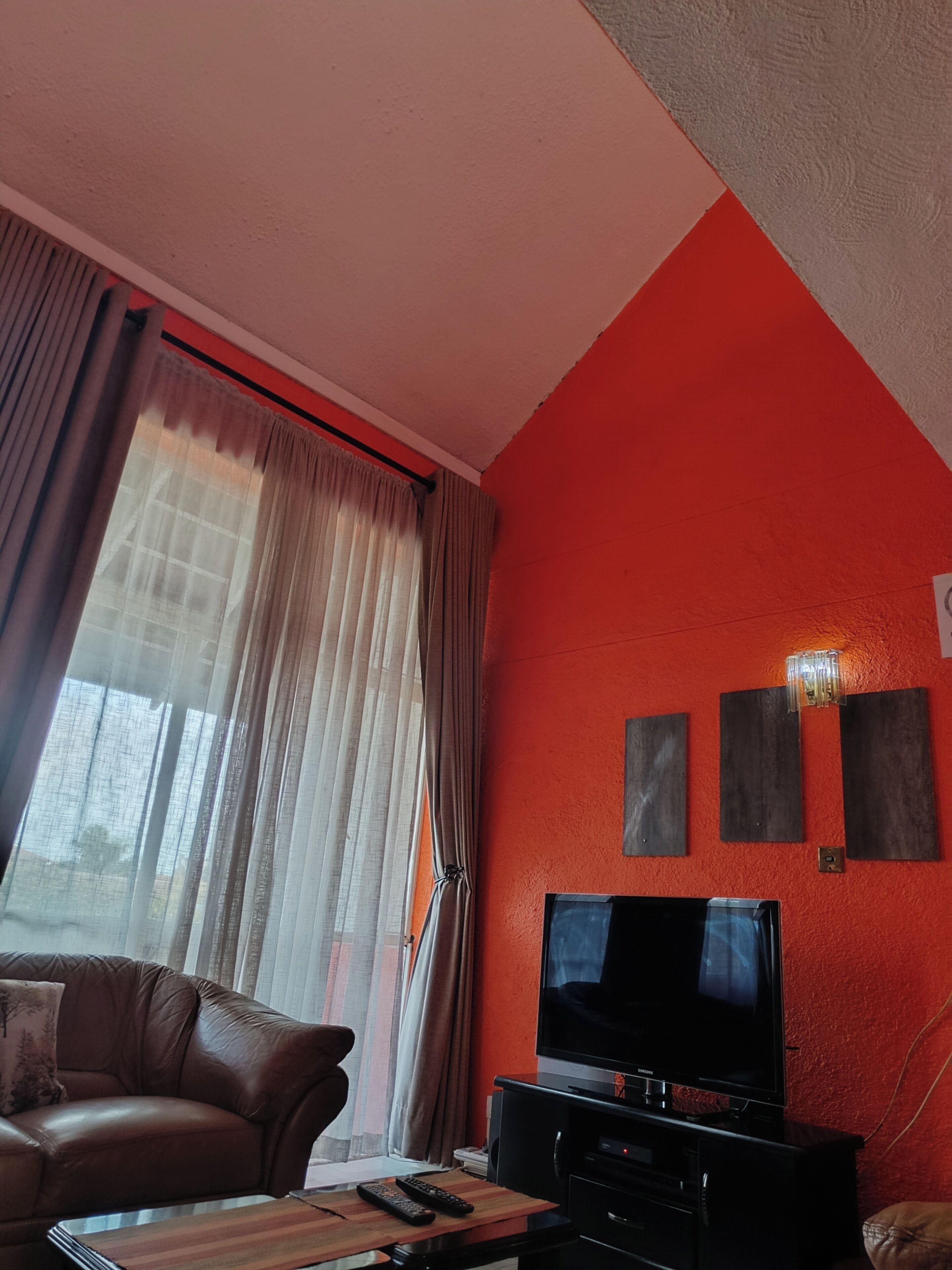 Una sala de estar con pared roja, un televisor de pantalla plana, un sofá de cuero y una ventana con cortinas.