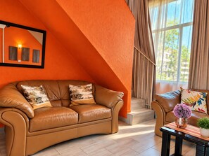 Una sala de estar moderna con un sofá de cuero color crema, una mesa de centro con un jarrón de flores y un ventanal con cortinas.