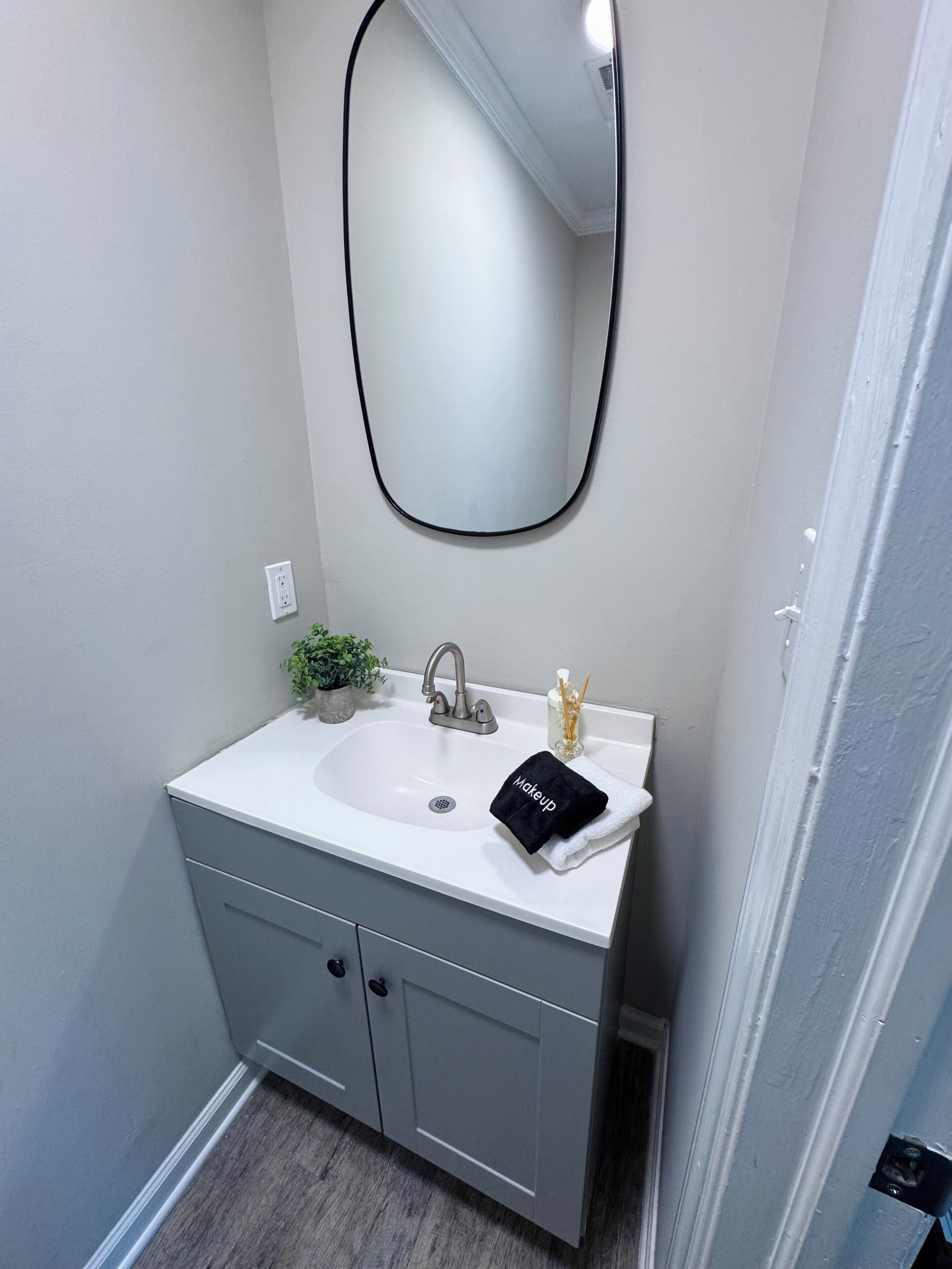 Un baño con un lavamanos blanco, un espejo, una planta pequeña y un perchero para toallas.