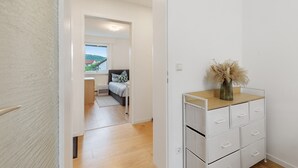 Un couloir mène à une chambre qui contient un lit, une table de chevet et une commode avec des tiroirs.