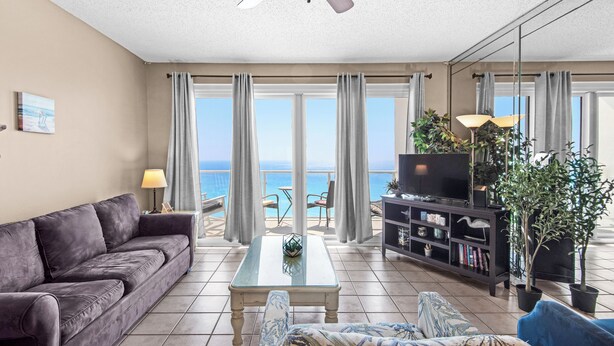 Ein Wohnzimmer mit Sofa, Couchtisch, Fernseher und einem Balkon mit Vorhängen.