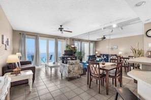 Ein geräumiger Wohnbereich mit Balkon, Deckenventilatoren, einem Esstisch und einem Fernseher.
