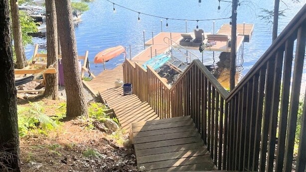 Una terraza de madera que da a un muelle con sillas y una mesa, con vistas a un lago.