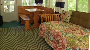 Interior de una cabaña con techo de madera, una mesa de comedor, un sofá y ventanas amplias con cortinas.