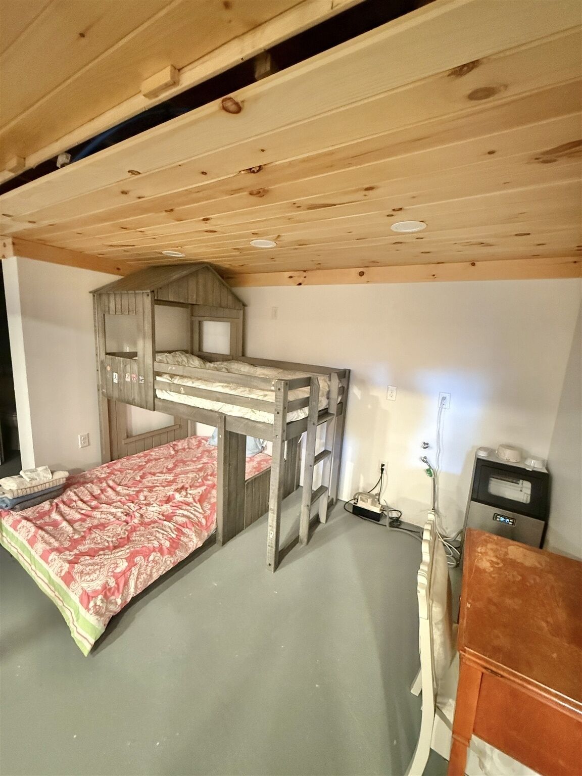 A bunk bed with a wooden headboard, a red patterned bedspread, and a small bedside table with a lamp.