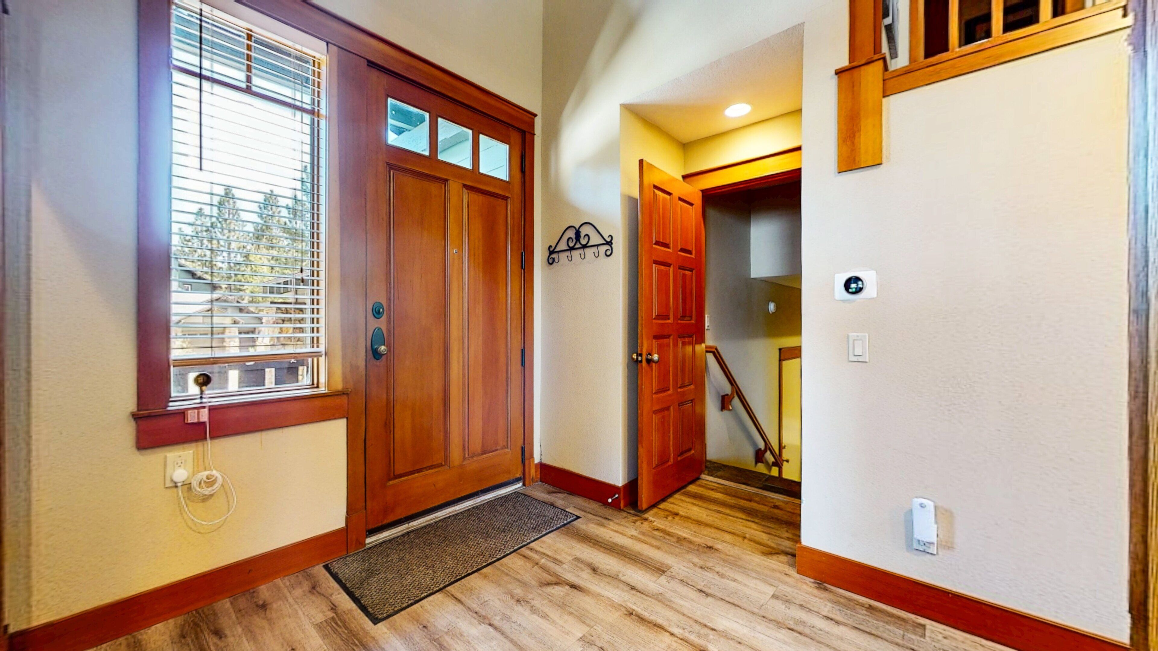 A wooden front door with a window, a doormat, and a wall-mounted light switch.