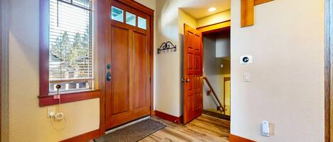 A wooden front door with a window, a doormat, and a wall-mounted light switch.