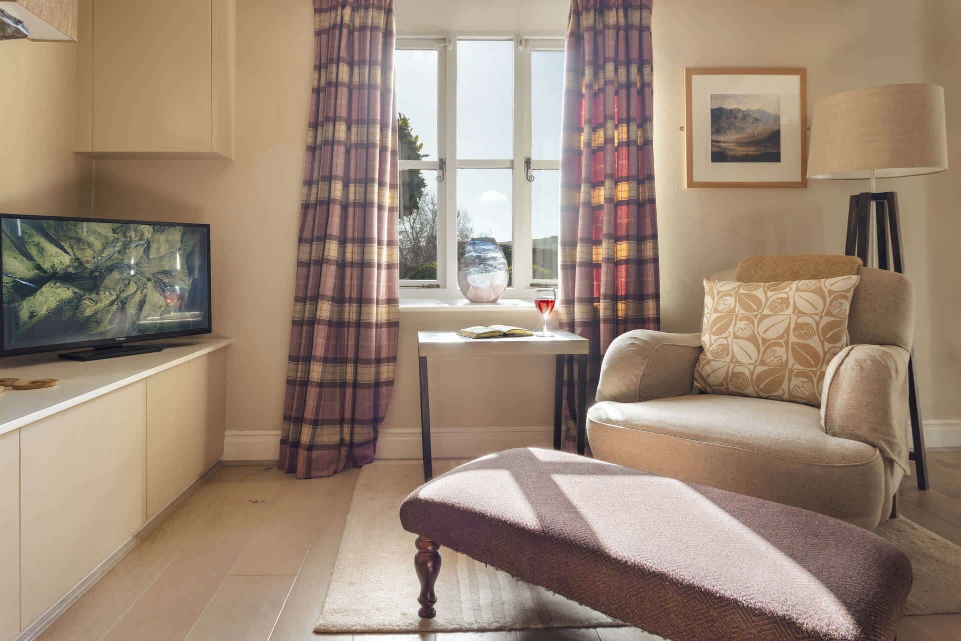 A living room with a television, a sofa, a table with a glass, and a window with curtains.