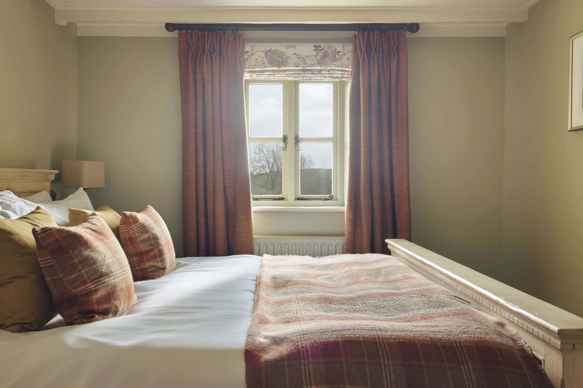 A bedroom with a bed, pillows, a window with curtains, a radiator, and a lamp.