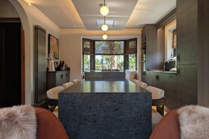 A modern kitchen with a central island, dark countertops, and a view of greenery outside.
