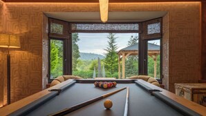 A pool table with a clear view of a forested landscape through large windows. - Wyke View | Ridgestone (Bowness-on-Windermere)