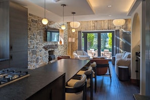 A modern kitchen with a stone wall, a large island, bar stools, and a dining area with a view.