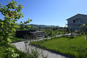 Ein Haus mit einem Kiesweg, der zu einer schwarzen Struktur führt, umgeben von Grünpflanzen und einem klaren Himmel.