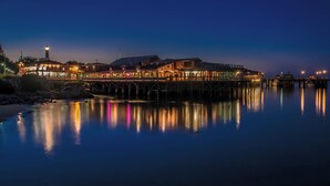 Un hôtel situé au bord de l’eau, doté d’un quai s’avançant dans l’eau, et comprenant plusieurs bâtiments illuminés ainsi qu’un phare imposant.