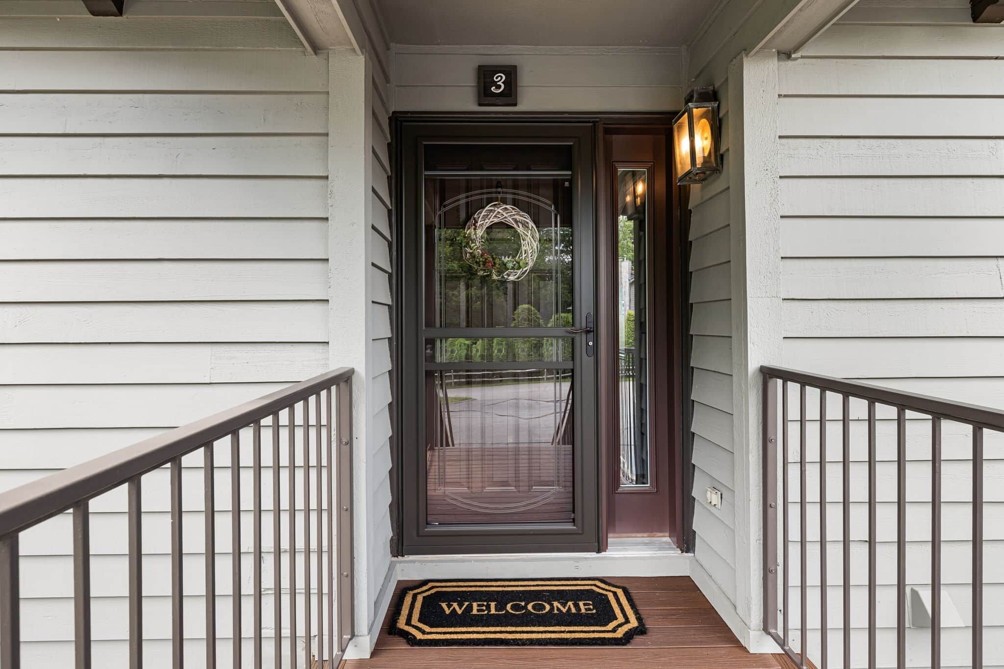 Une entrée de maison avec une porte sombre, un paillasson et un panneau portant le chiffre « 3 » au-dessus de la porte.