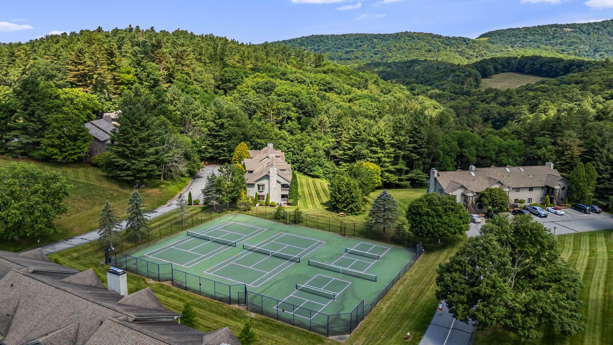 Ein Wohngebiet mit Tennisplatz, umgeben von Häusern und dichtem Wald.