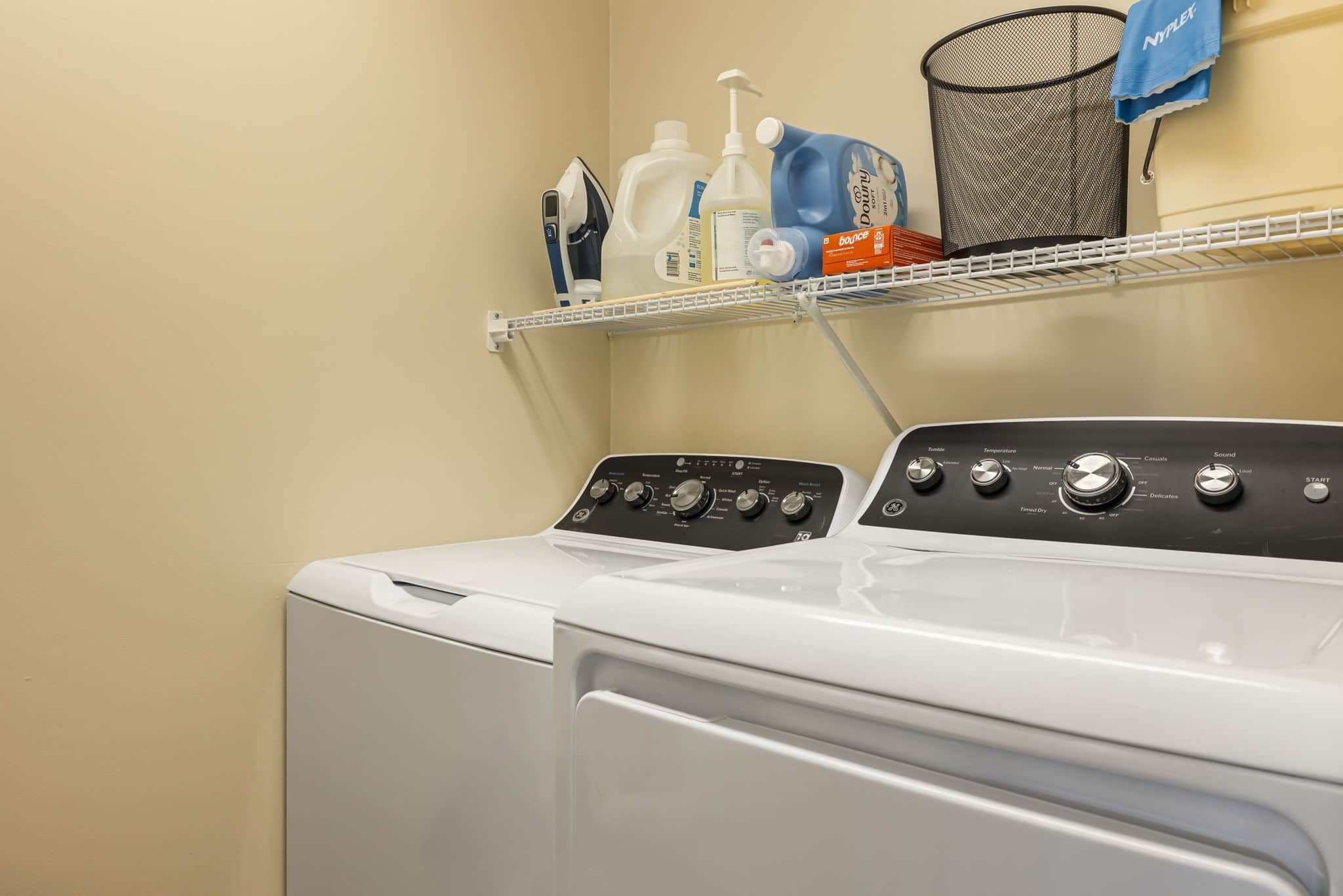 Un lave-linge à chargement frontal doté d’un panneau de commande, d’une étagère au-dessus pour ranger les produits de lessive et d’un panier à linge contenant une serviette.